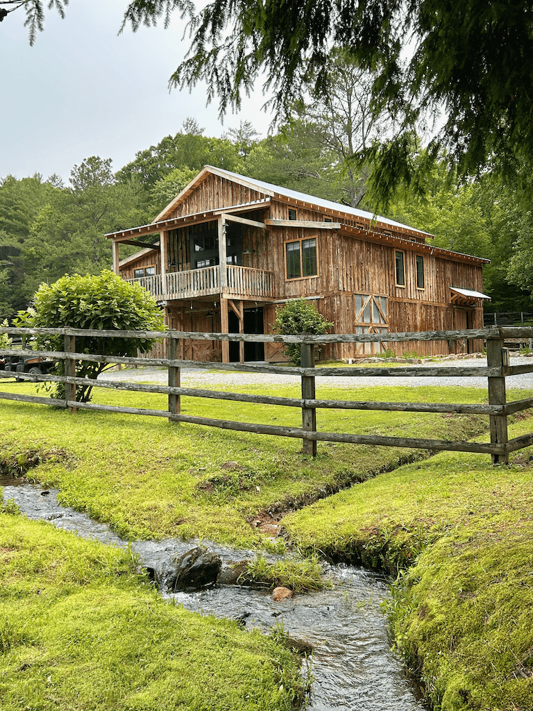 A small creek along the property's split-rail fence line, with the barn visible in the background