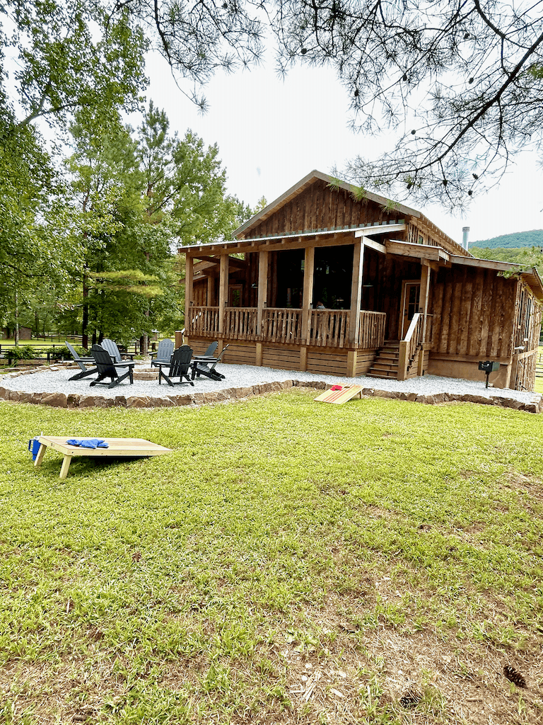 Open lawn in front of the barn with adirondack chairs around a fire ring and a cornhole board set up on the grass