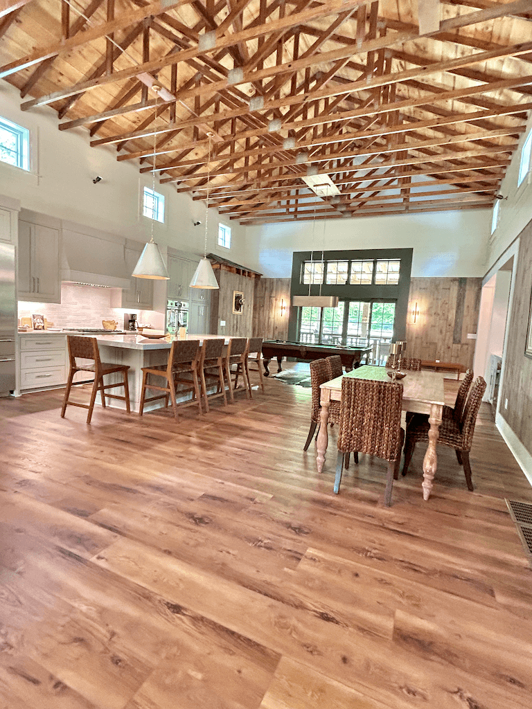 Open floor plan at The Barn — vaulted ceilings with exposed wood trusses, kitchen and dining table flowing into one airy space