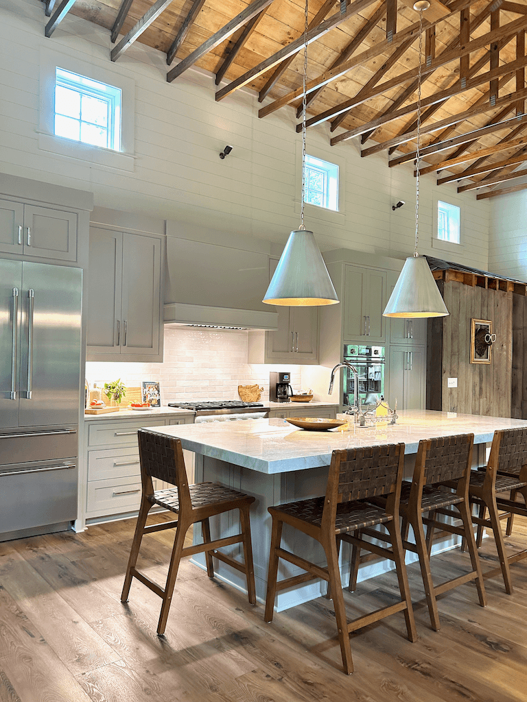 The kitchen island at The Barn — long stone-topped island with bar seating, pendant lighting, and a chef's range against the back wall