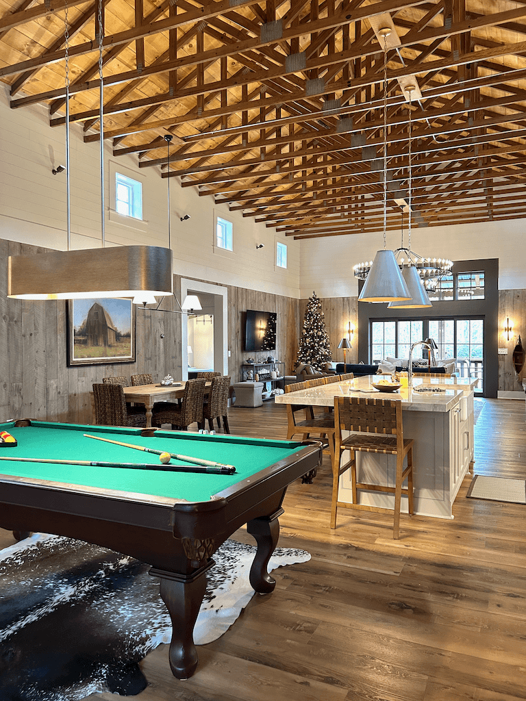 The billiards and game space — full-size pool table, cathedral beams overhead, light flooding in from the back windows
