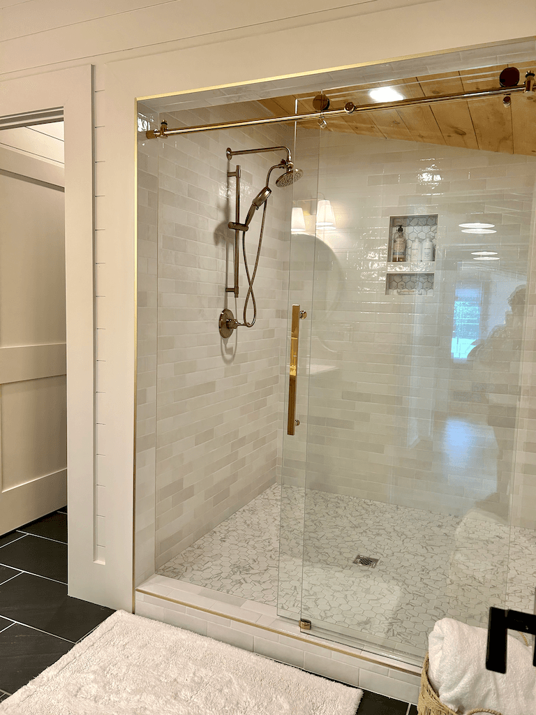 Master bath at The Barn — walk-in shower with stone-tile surround, brushed fixtures, and natural light