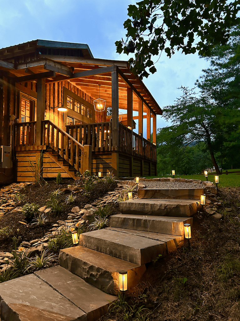 The Barn at Haynes Hill at night — porch lights and interior glow against a deep blue sky, lit stone steps leading up to the entry